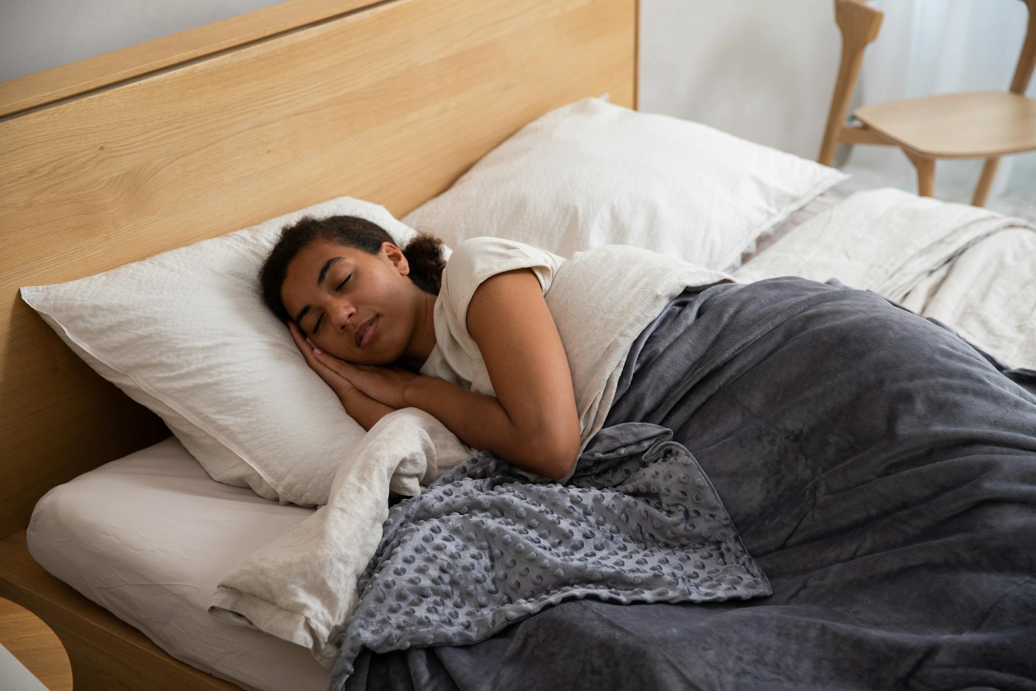 A woman peacefully sleeping in bed using a cozy weighted blanket, promoting relaxation.